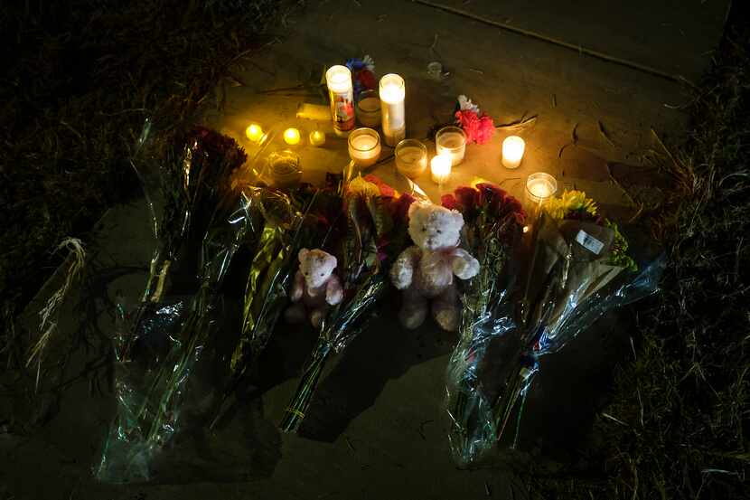 Flowers, candles and teddy bears rest on the sidewalk in the front yard of the house where...
