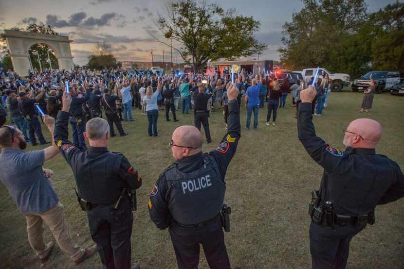 Mourners and Haltom City police officers hold glowsticks during a candlelight memorial for...