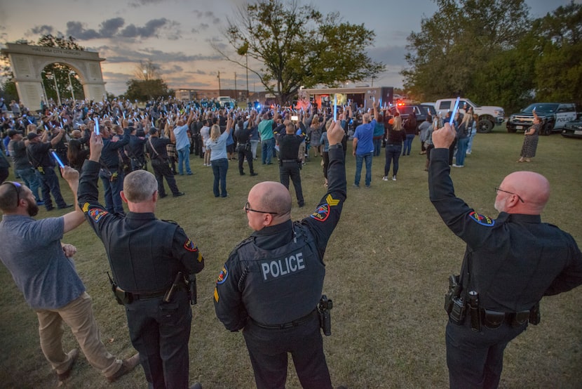 Mourners and Haltom City police officers hold glowsticks during a candlelight memorial for...