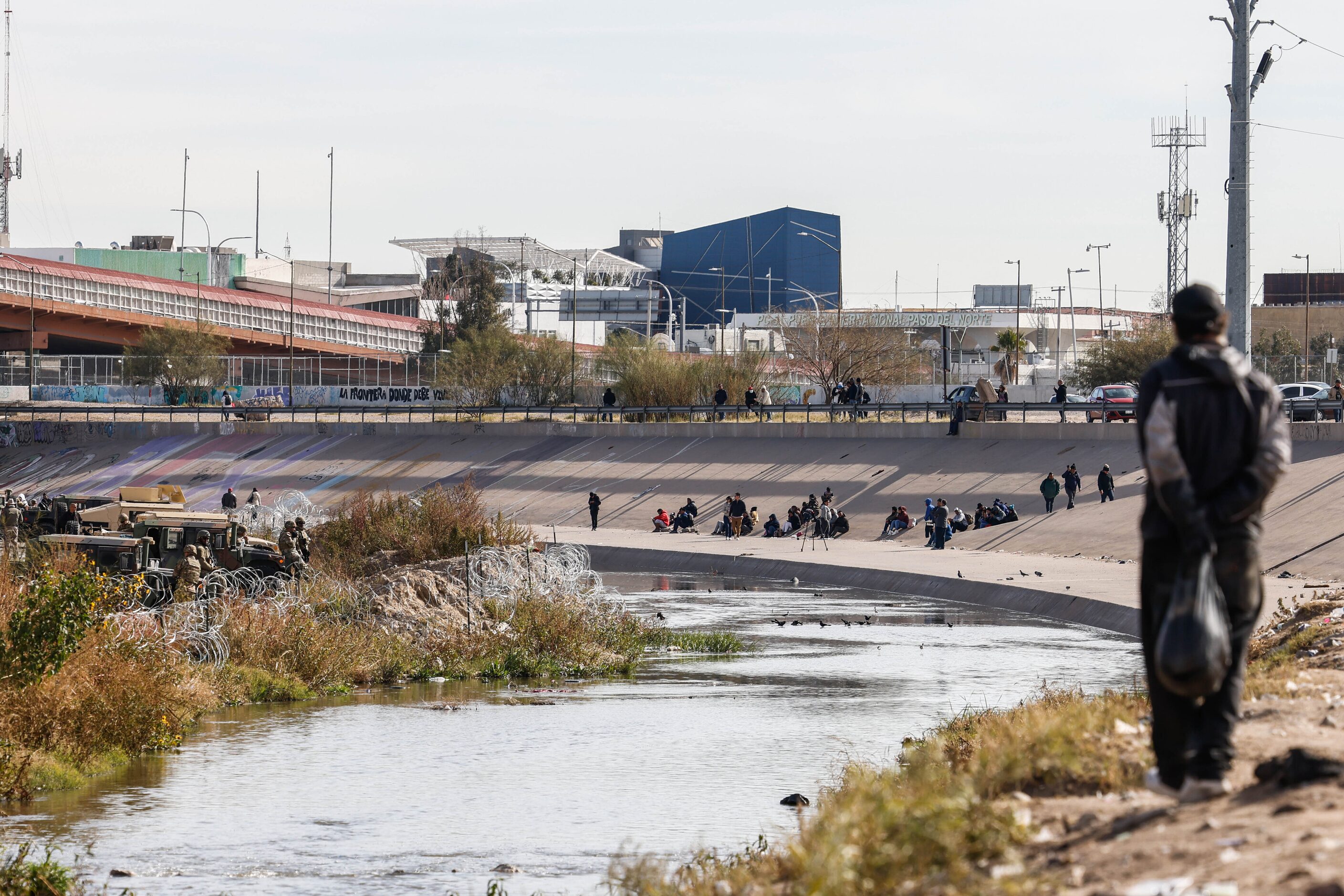 A group of migrants observe the situation at the other side of the border as seen from...