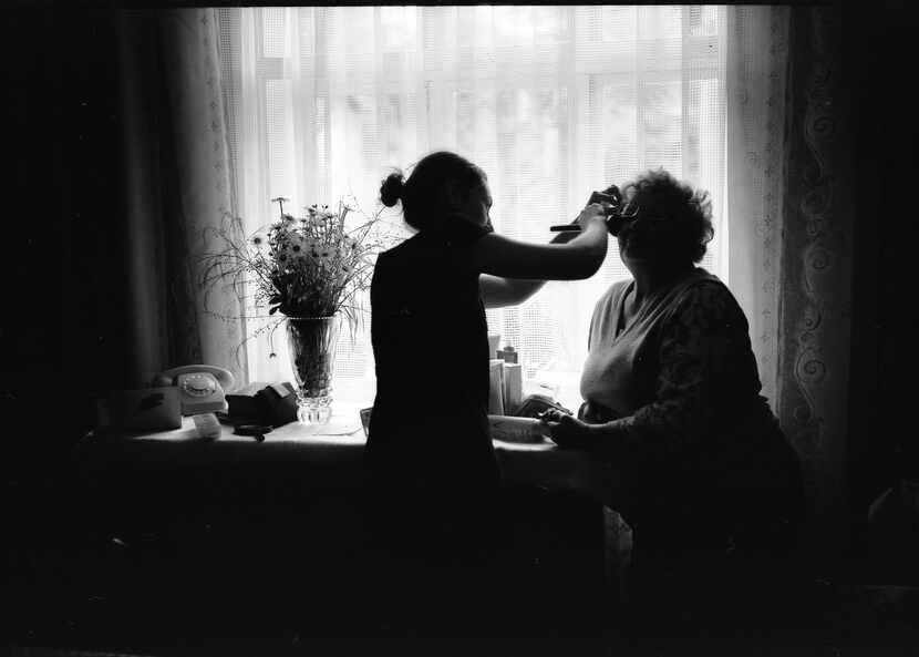A caregiver helps an elderly woman put on makeup in her room.