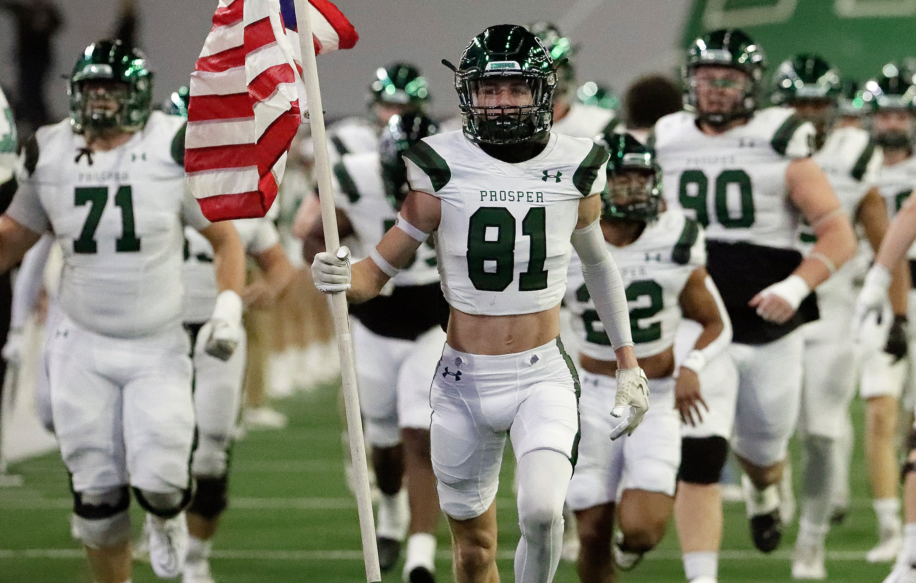 Prosper High School wide receiver Cohen Newsholme (81) carries a U.S. flag onto the field...