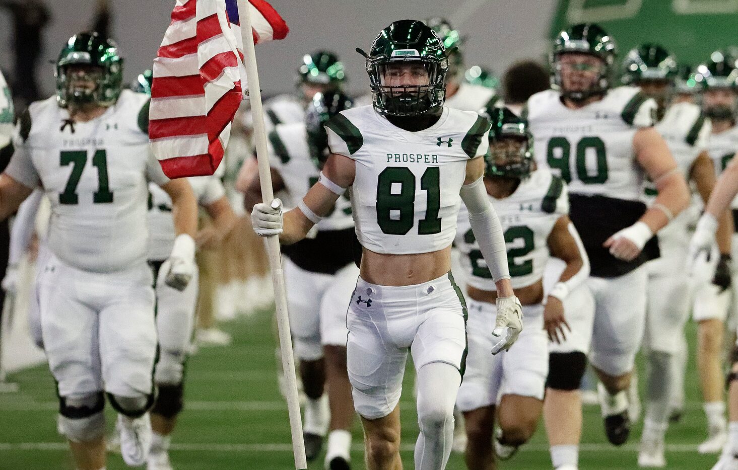 Prosper High School wide receiver Cohen Newsholme (81) carries a U.S. flag onto the field...