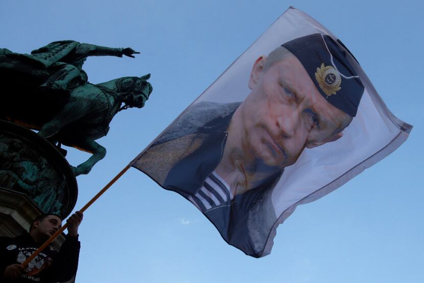 A man waves a flag showing Russian President Vladimir Putin in front of the monument of late...
