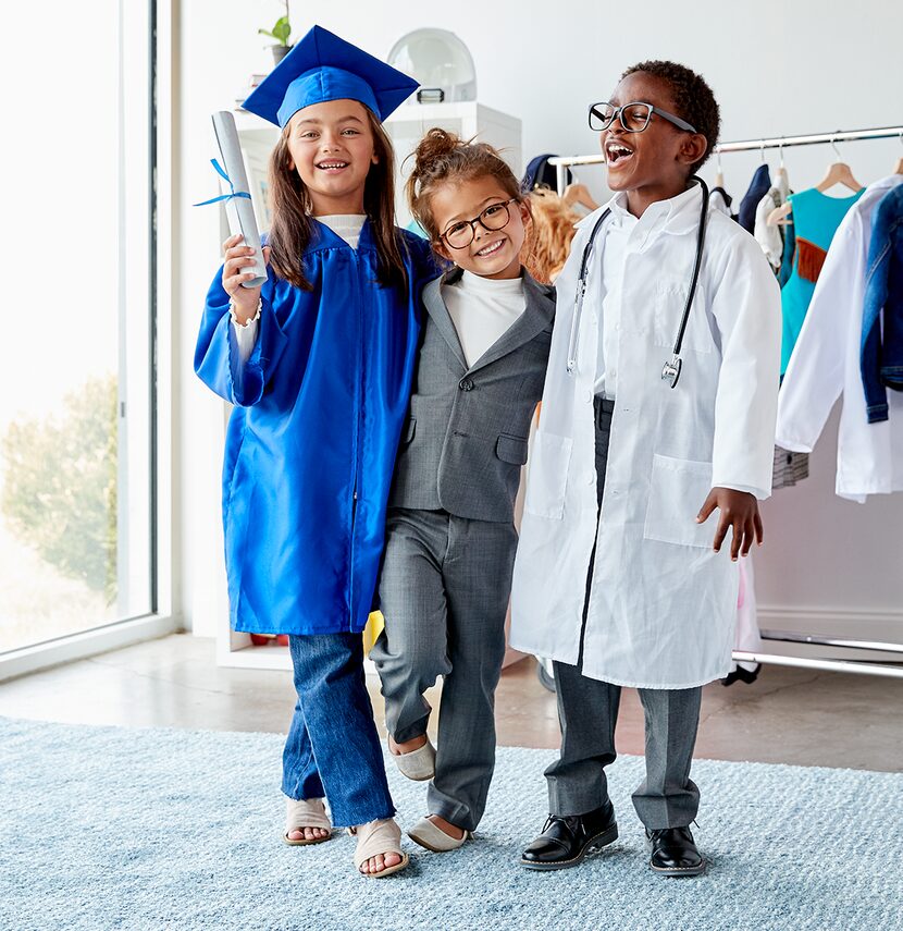 Three young children dressed up as a graduate, a business woman and a doctor smile and pose...