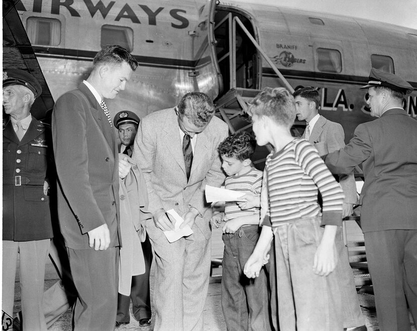 University of Oklahoma coach Bud Wilkinson bends over to sign an autograph for a young fan...