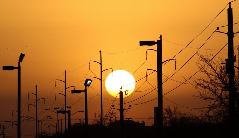 Overhead power lines and light poles are silhouetted as the morning sun rises over Camp...