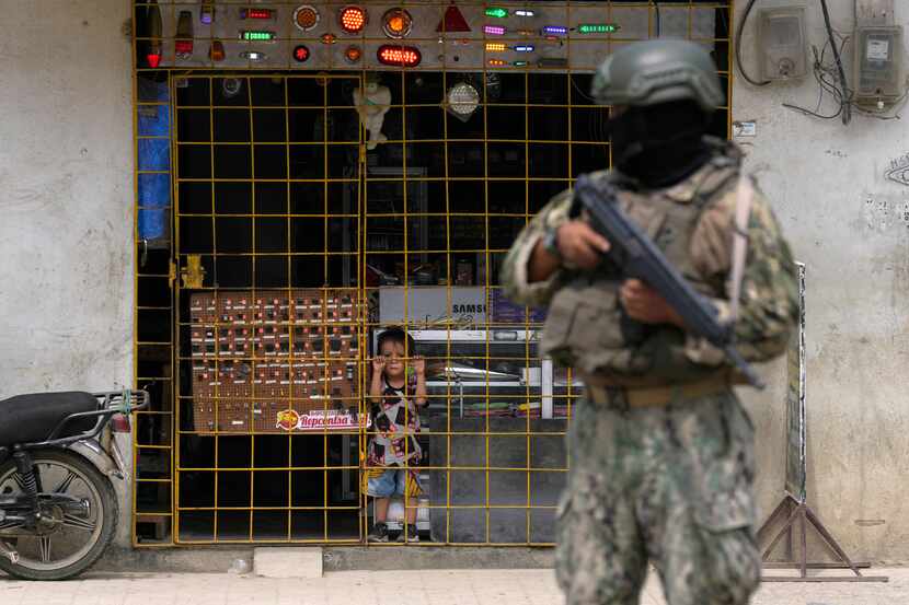 A boy watches from behind the bars of an open electronics store as a soldier stands guard at...