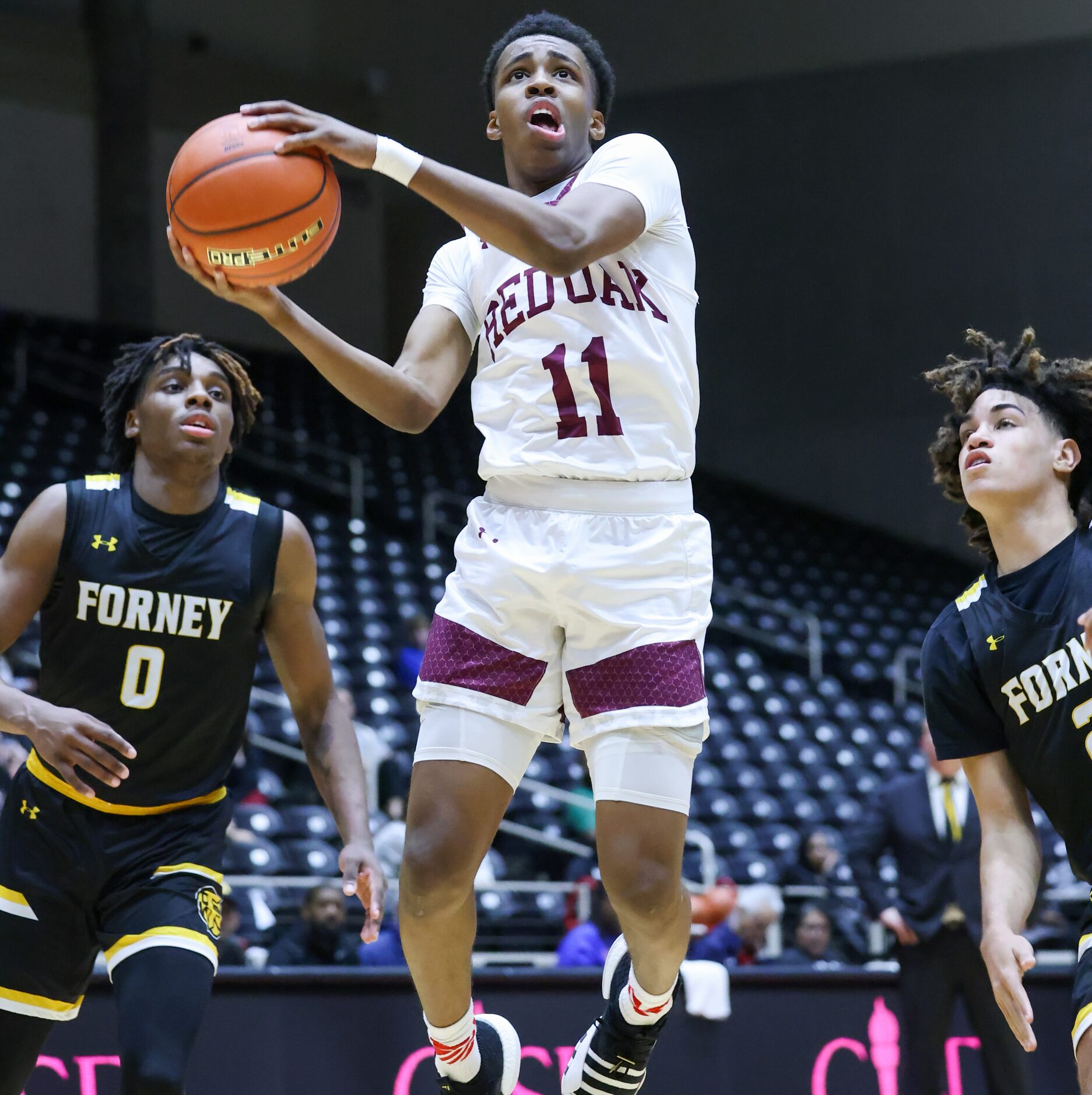 Red Oak freshman guard Michael Gatewood (11) jumps as he nears the net, trailed by Forney...