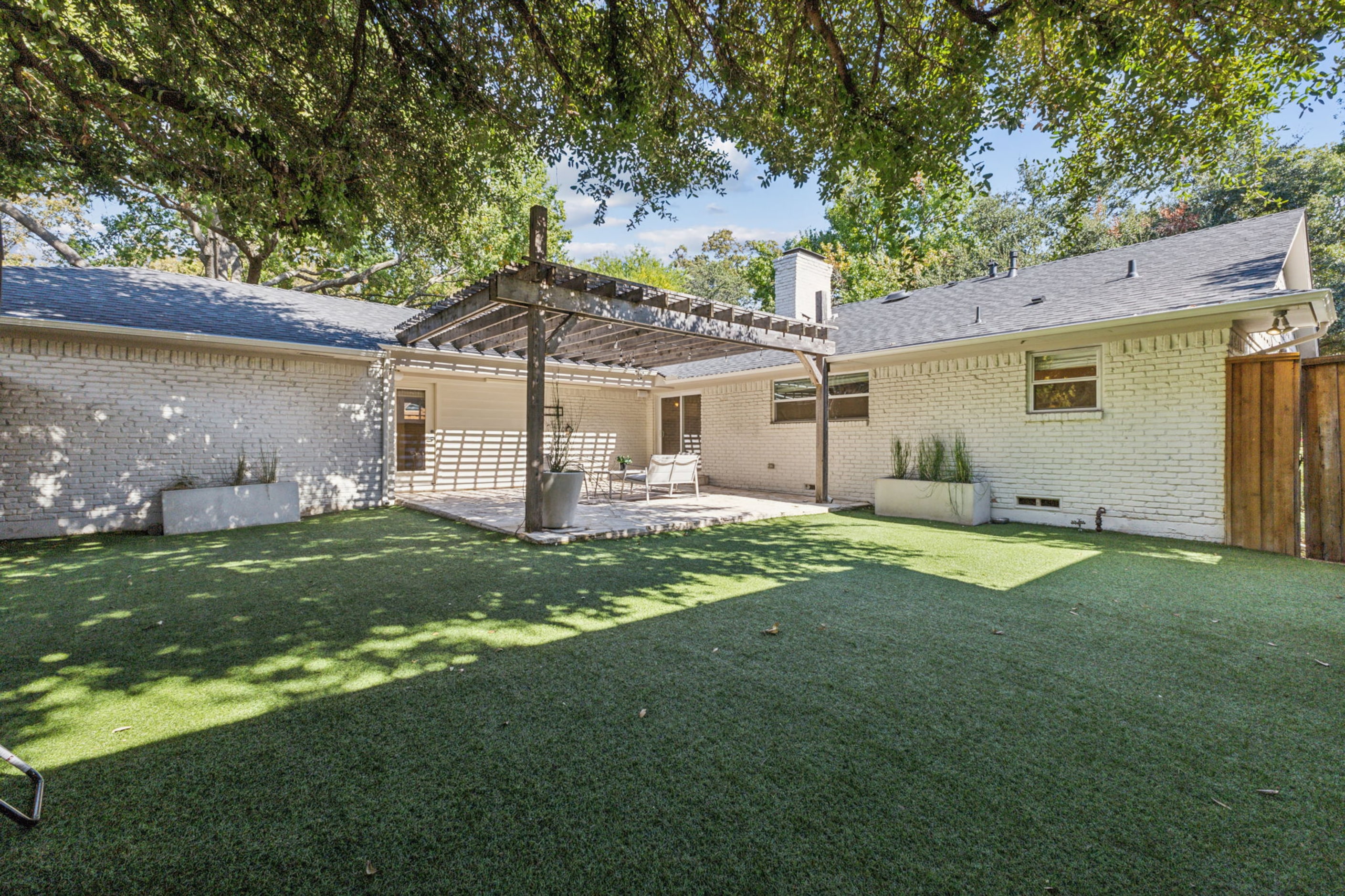 In the backyard, a patio with a pergola offers a place to lounge, while a turfed lawn offers...