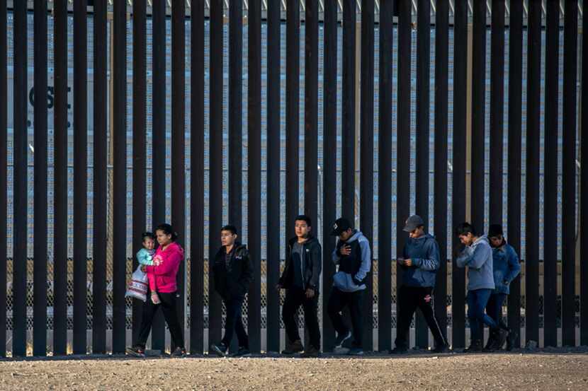 Undocumented immigrants walk along the U.S.-Mexico border wall after running across the...