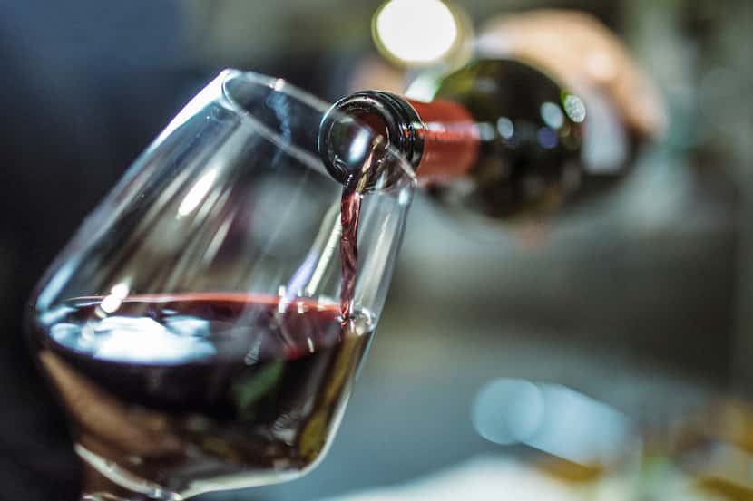 Unrecognizable person, holding a bottle of red wine, is pouring some red wine in a wine glass.