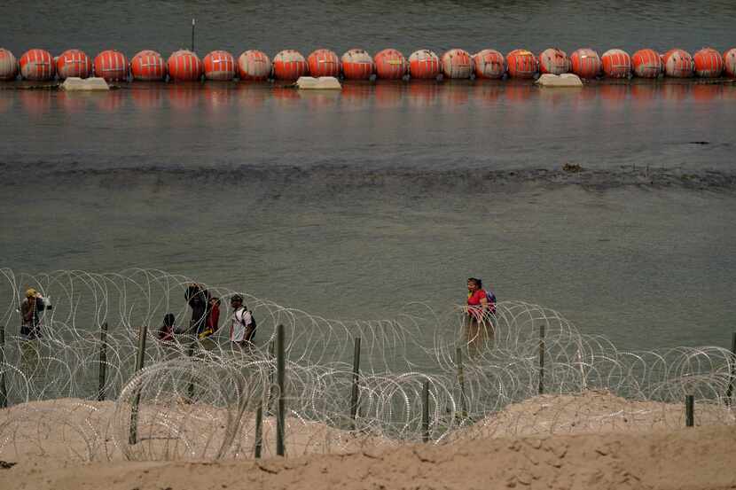 Migrants from Columbia walk along Concertina wire and a floating buoy barrier after crossing...