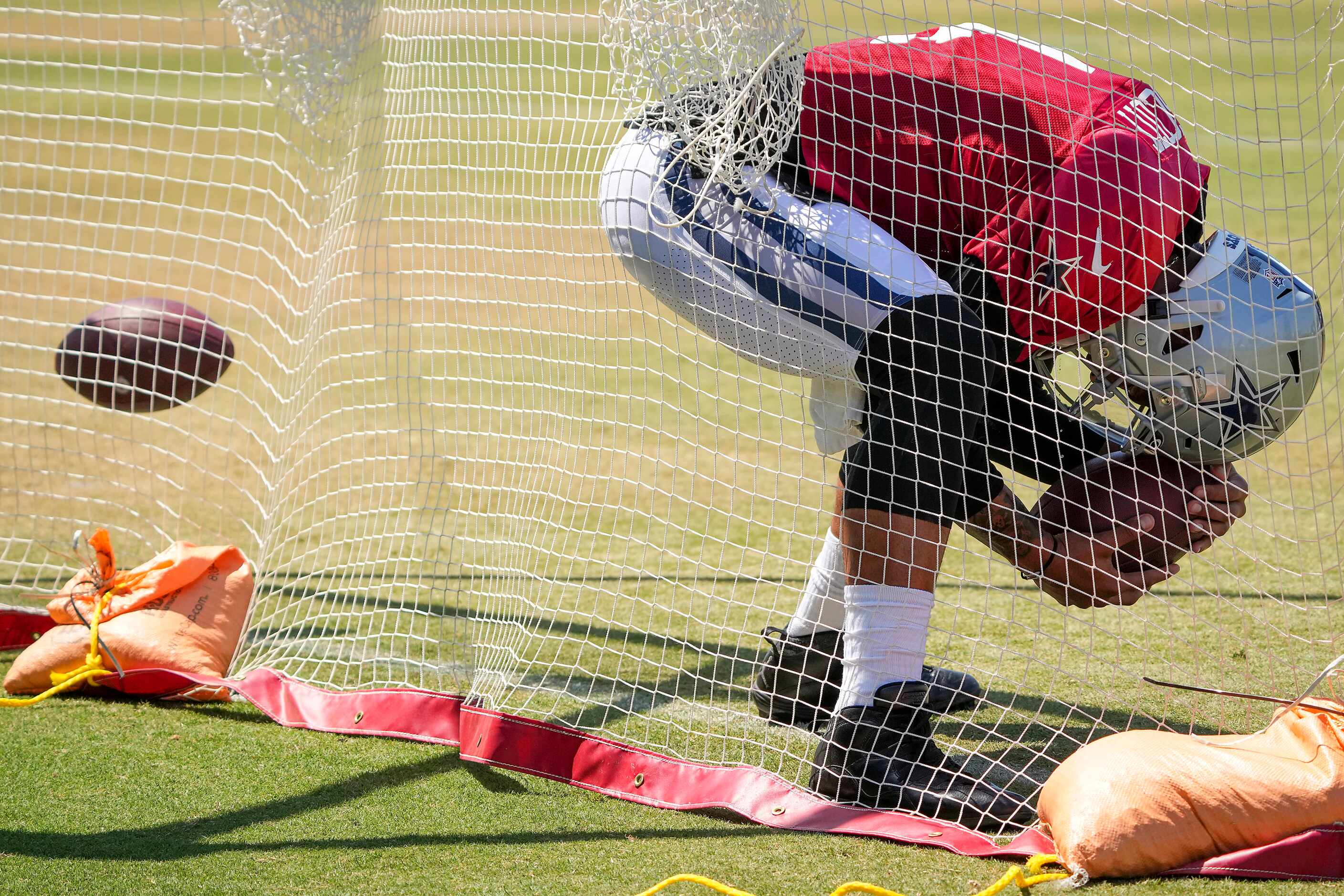 Dallas Cowboys quarterback Dak Prescott ducks under a pass as he retrieves a ball from a net...