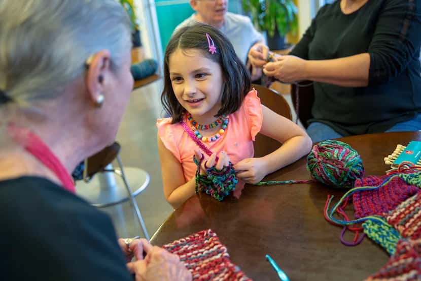Sophie McKinney, 6, asks Arlene Leibs how many scarves she has made during the Spreading the...