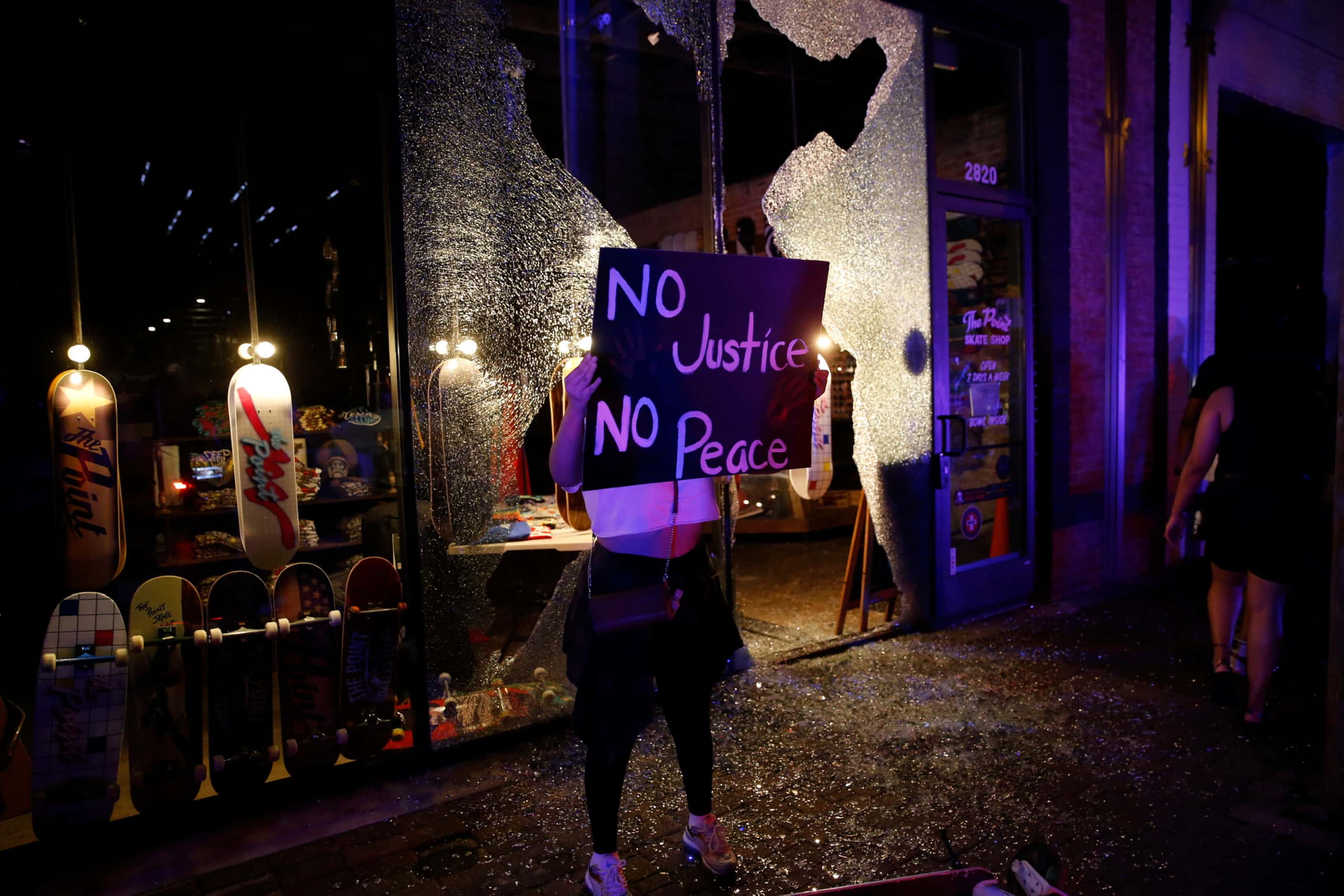 A protestor passes by broken windows along Main Street in Deep ellum after protesters passed...