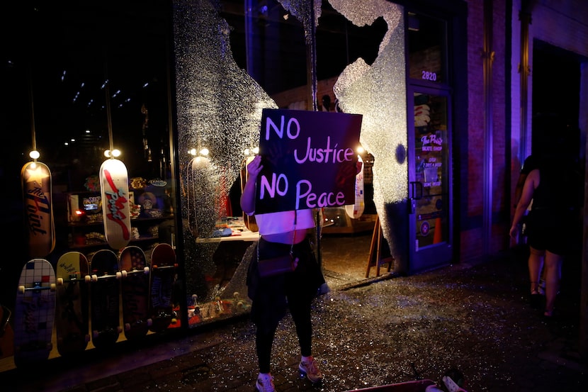 Una persona pasa frente a la ventana rota de un negocio en Main Street, en Deep Ellum, junto...