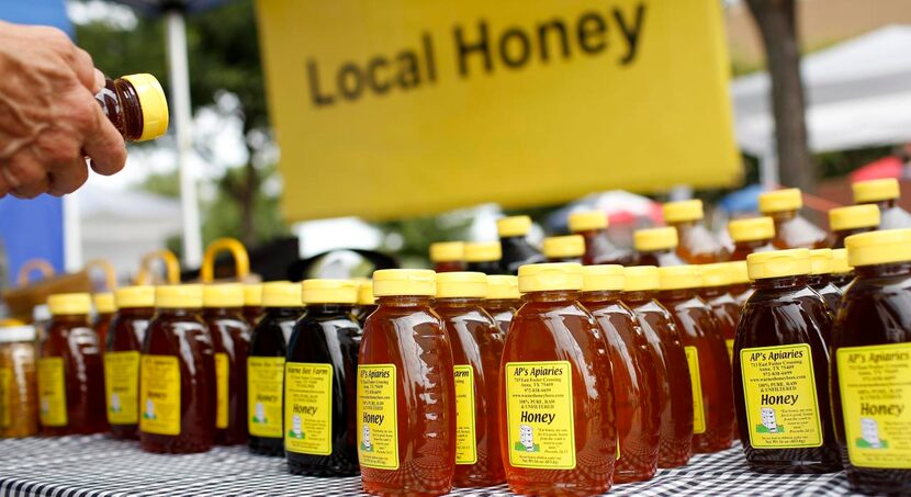 
Jars of local raw honey line a table. Neighboring them were sticks of flavored honey in...