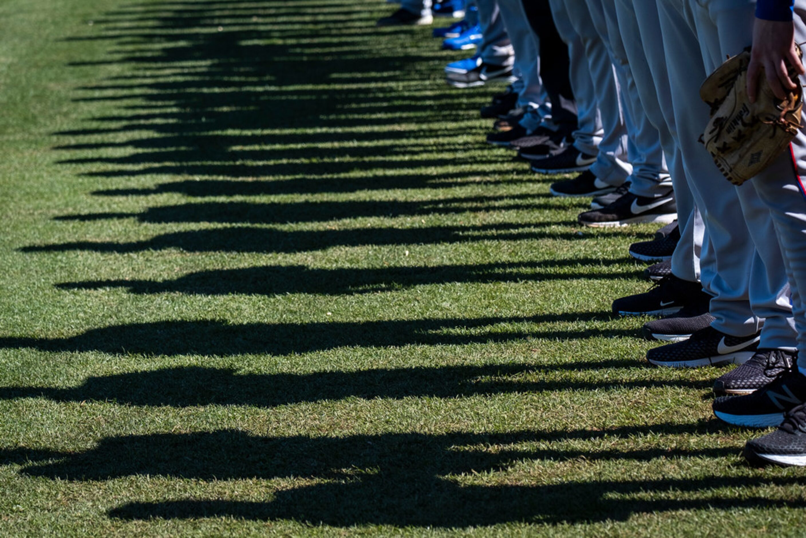 Texas Rangers cast shadows on the field as they stand for the national anthem before a...