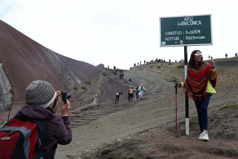 A tourist poses for a photo at the entrance that leads to Rainbow Mountain, in Pitumarca,...