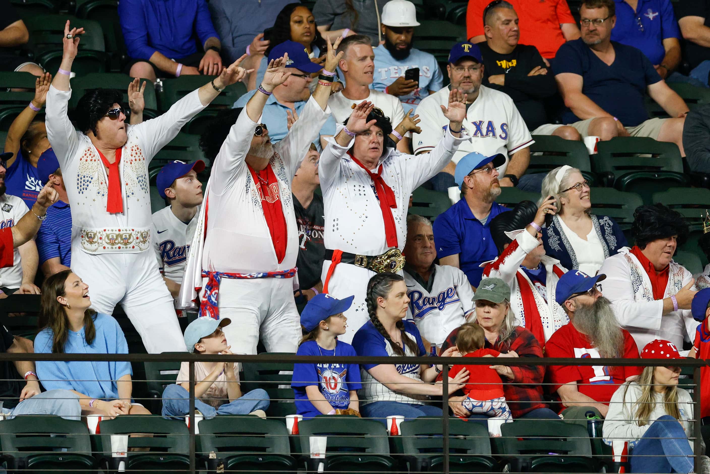 A group of Texas Rangers fans dressed as Elvis Presley stand and dance during a game against...