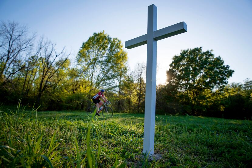 Sun sets behind a white cross in memory of David Stevens along White Rock Creek Trail...