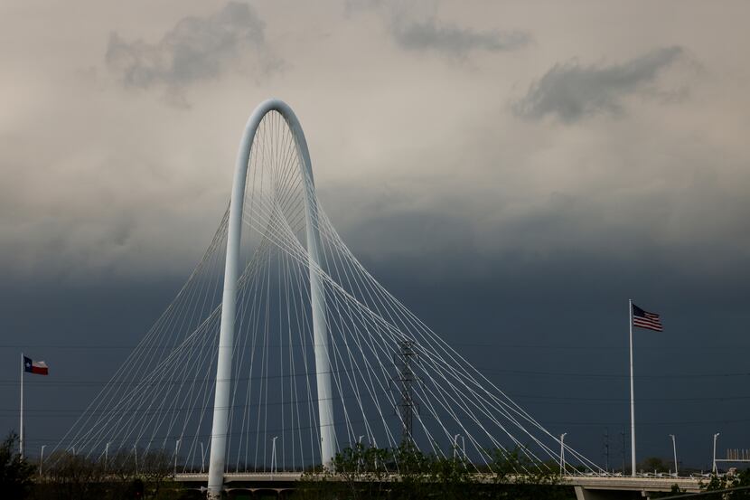 Flags on Margaret Hunt Hill Bridge ripple in the wind as storm clouds move toward downtown...