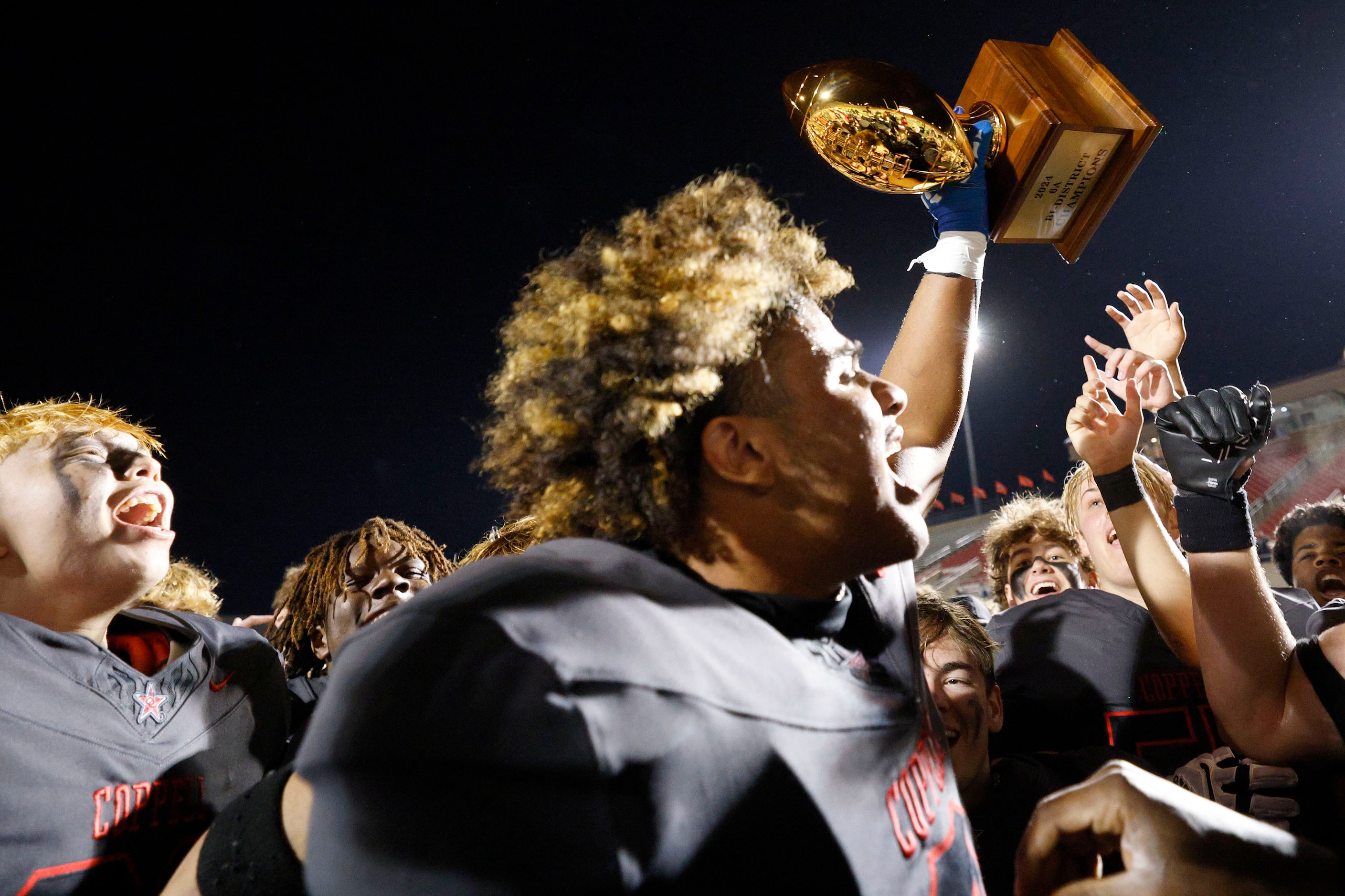 Coppell's Titus Roberson (0) holds up a trophy as his teammates celebrate their 35-27...