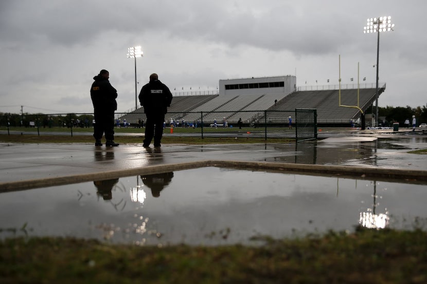 Security guards stand in between rain showers before a high school football game between...