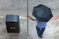 A man waits for a DART bus under an umbrella as rain falls in downtown Dallas, Wednesday,...