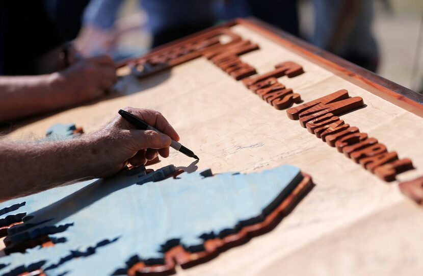 Joe Joplin of North Texas Municipal Water District signs a wooden board with a carved out...