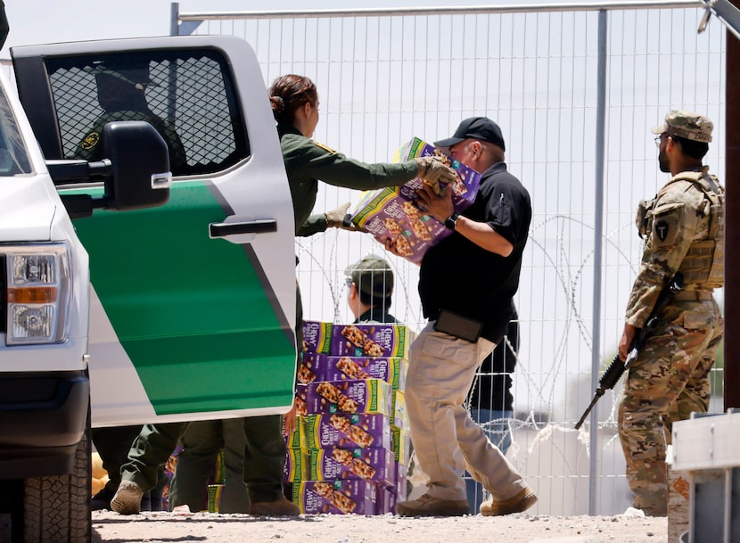 Customs and Border Patrol staff unload large boxes of trail mix bars (and water) for migrant...