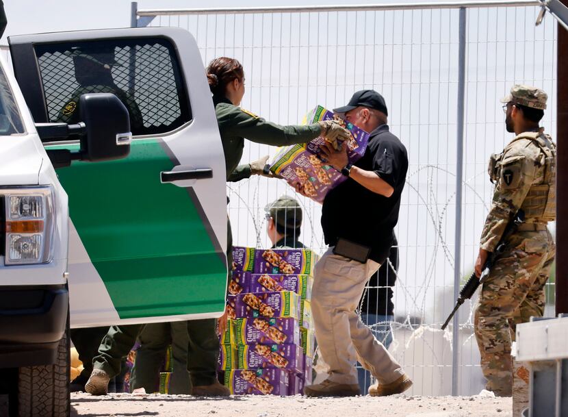 Customs and Border Patrol staff unload large boxes of trail mix bars (and water) for migrant...