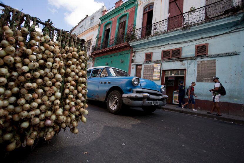 A classic American car passes by a stall selling onions in Havana, Cuba, Wednesday, Dec. 17,...