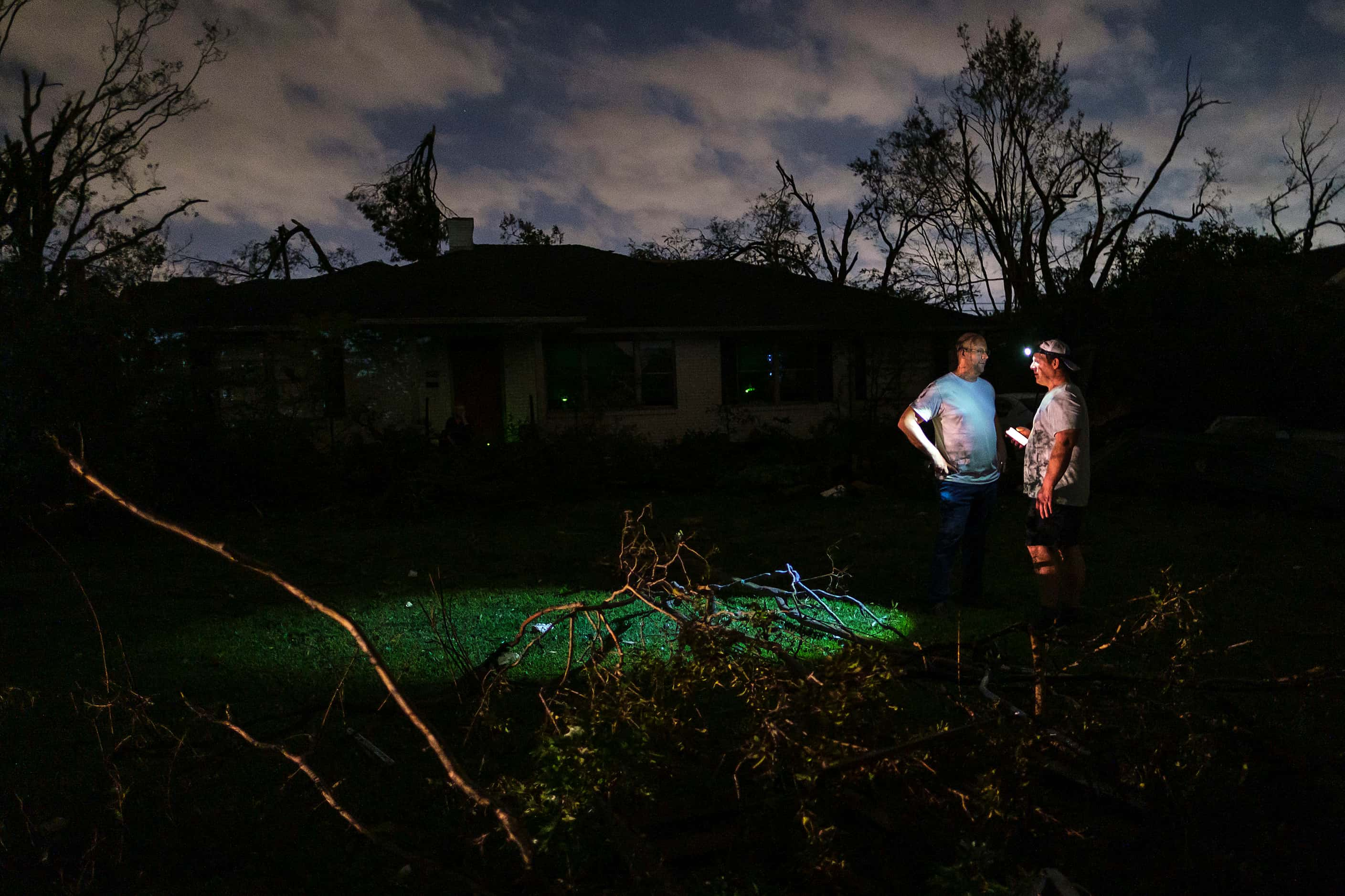 Residents survey tornado damage to their darkened neighborhood near the intersection of...