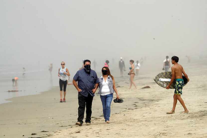 People wear masks as they walk on the beach Sunday, April 26, 2020, in Huntington Beach,...