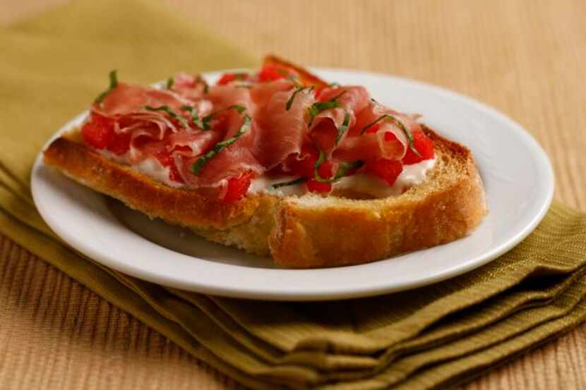 
Diced fresh watermelon lies between goat cheese and prosciutto on toasted sourdough bread. 
