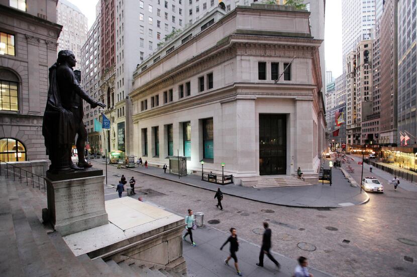 FILE - In this Oct. 8, 2014, file photo, people walk to work on Wall Street beneath a statue...