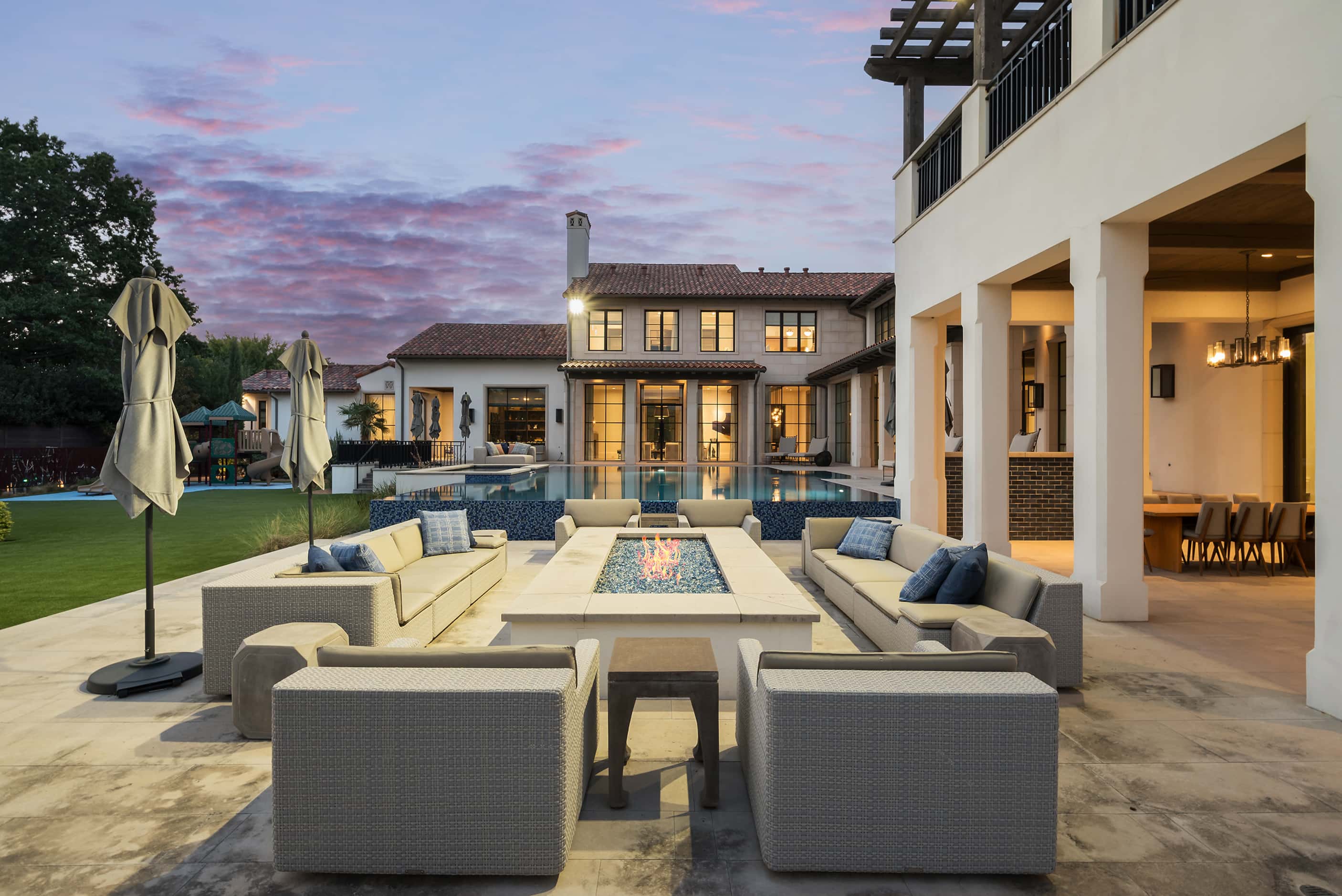 An evening scene in a backyard shows an outdoor seating area, a pool and the house in the...