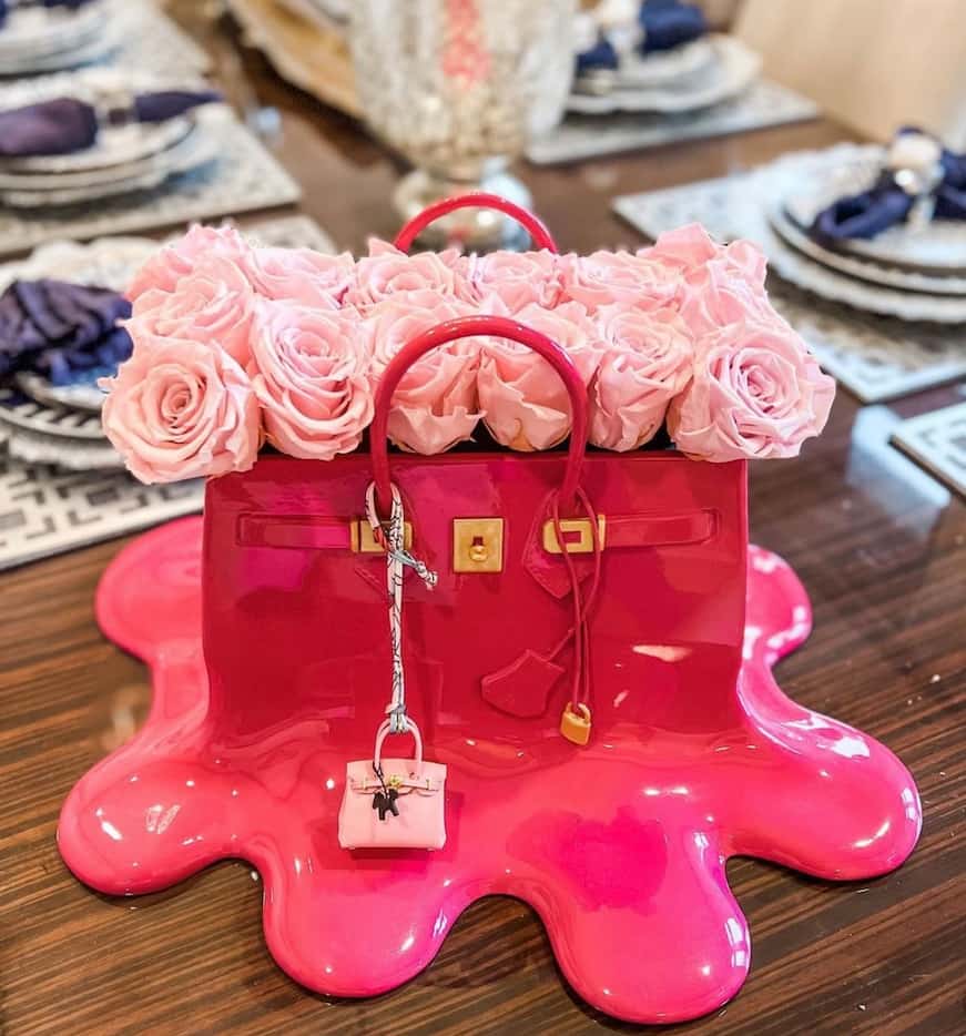 Sculpture of melting pink handbag on a table with two rows of light pink roses inside