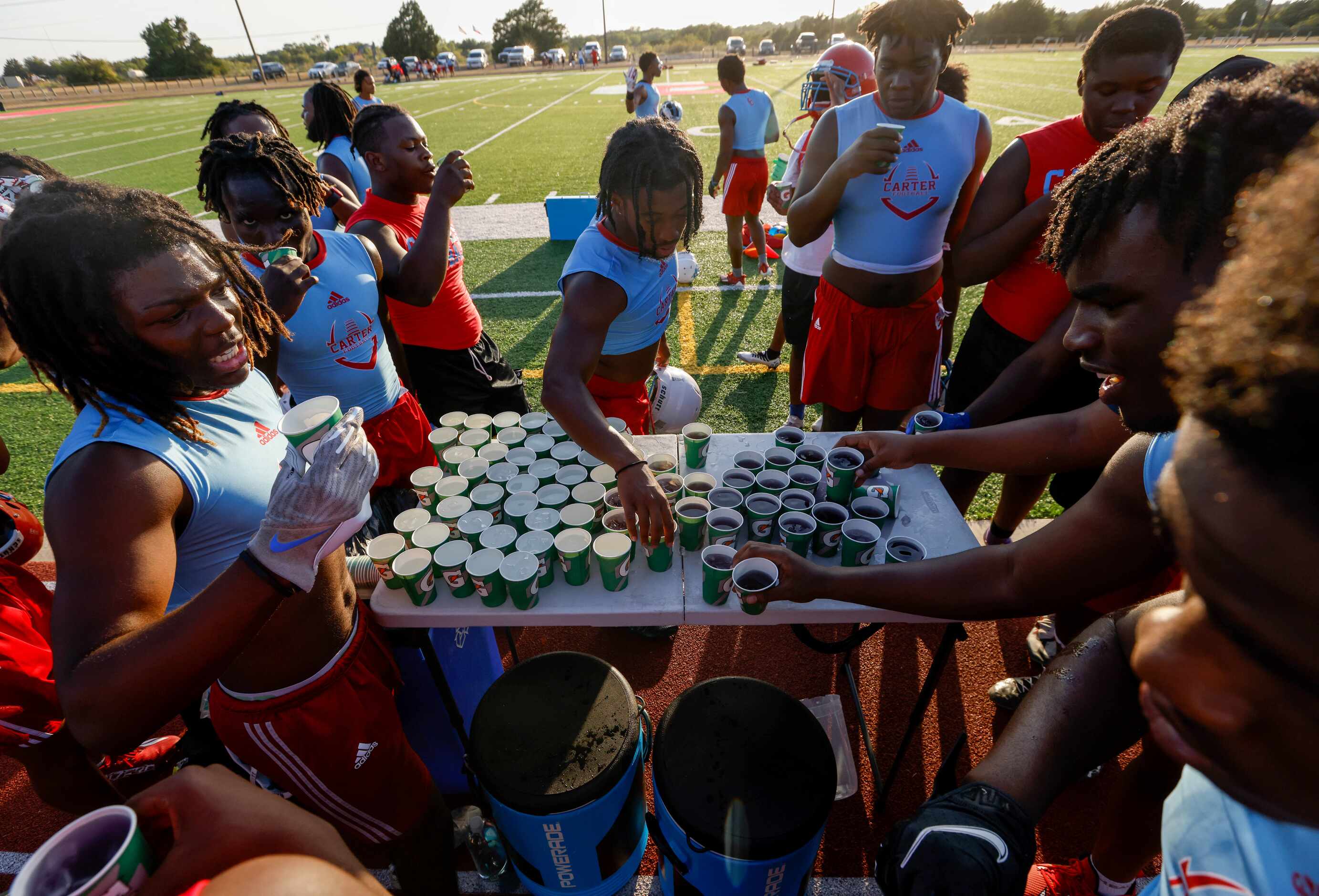 Players crowd around a table with Gatorade and water at Carter High School during a break in...