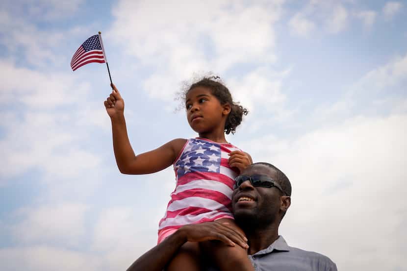 Eve Darlington, 6, waves a flag from atop the shoulders of her father, Dan Darlington, as...