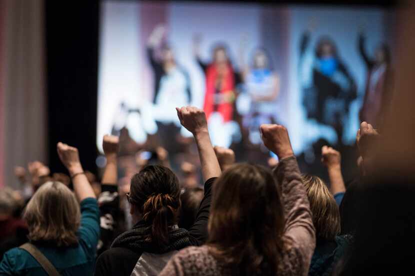 Attendees raise their fists as they hear the opening prayers song offered by five indigenous...