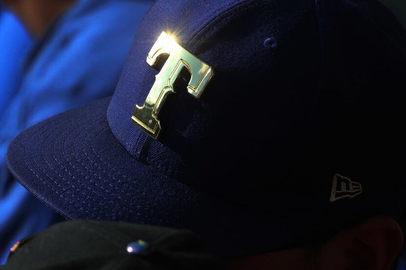 FILE - The sun glints off a metallic Rangers logo on a fan's hat during a game between the...