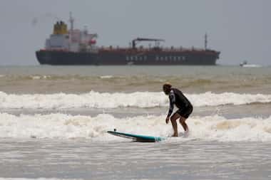 An oil tanker heads out to open water as a surfer takes advantage of waves ahead of...