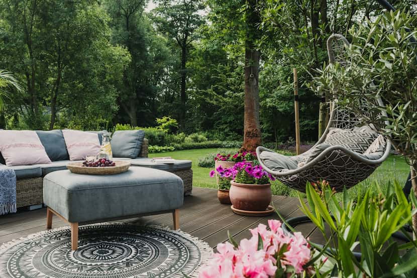A deck with pots of colorful pink cyclamen and petunias, a cozy couch and ottoman, a basket...
