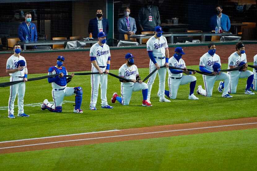 Texas Rangers players alternately stand or kneel while holding a black fabric before the...
