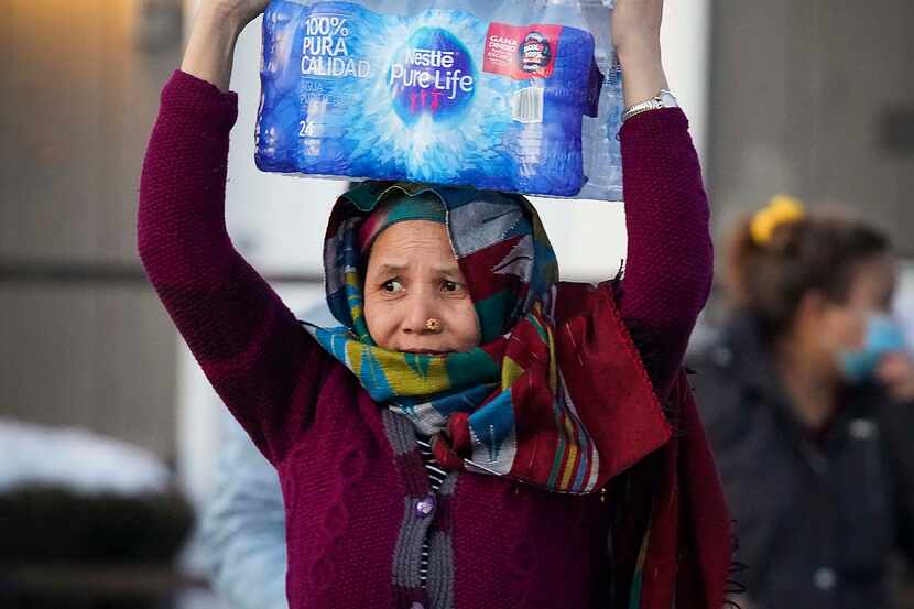 A woman carries two cases of drinking water distributed at the Literacy Achieves nonprofit...