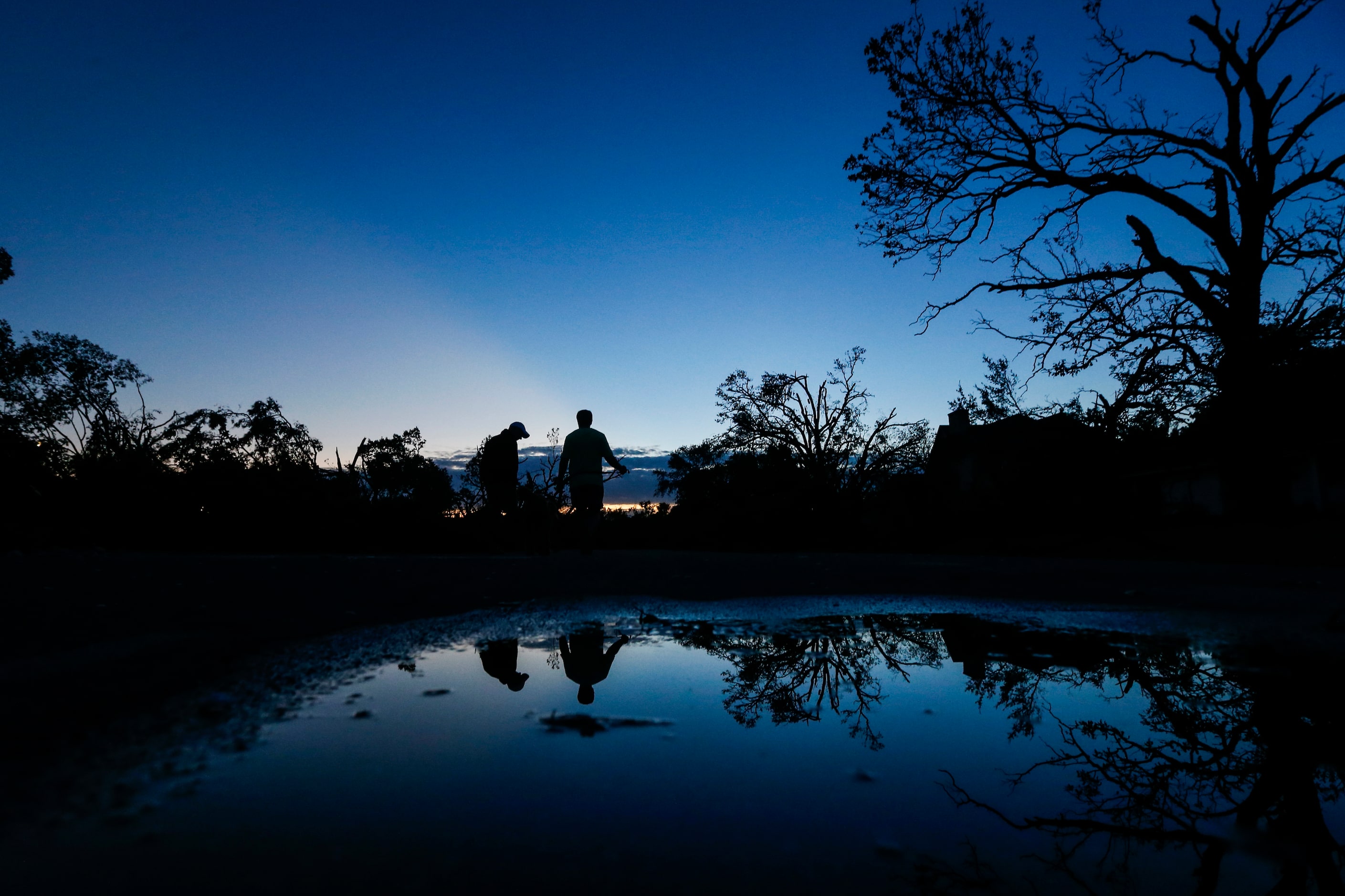 As the sunrises, homeowners Dennis Gambow, left, and Eric Charton emerge to survey damage...