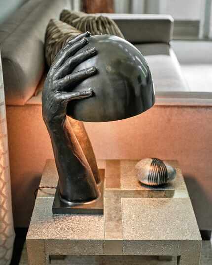 A bronze lamp has a unique design with two hands grasping a dome. The lamp is set on a table...